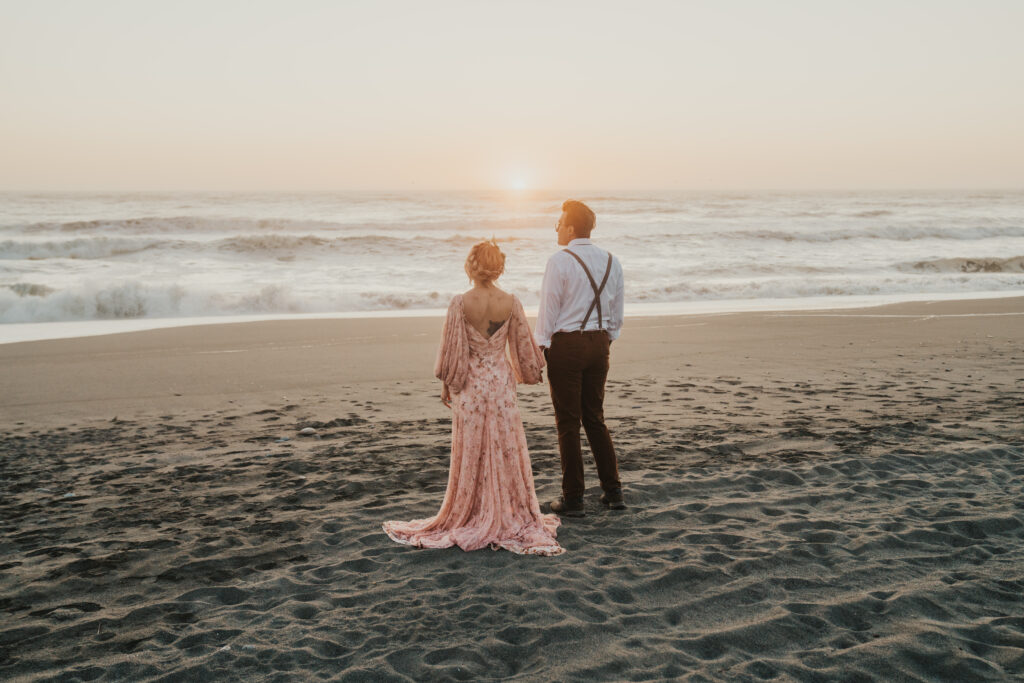 Big Sur elopement photo of bride and groom standing together on beach looking out at the ocean