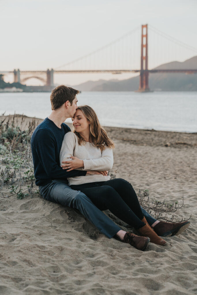 Couple sitting in the sand on the beach in front of golden gate bridge