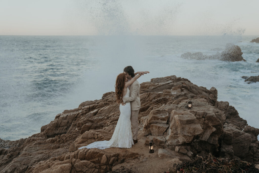 Bride and groom kissing as wave splashes behind them at Big Sur elopement in Garrapata State Park