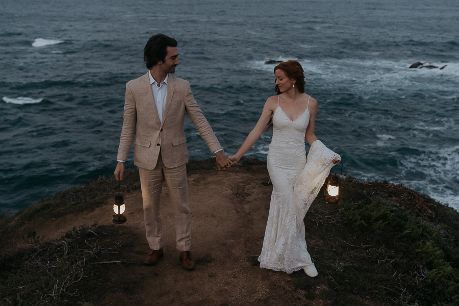 bride and groom holding hands standing apart and looking at each other while holding lanterns in front of the ocean on the Big Sur coast