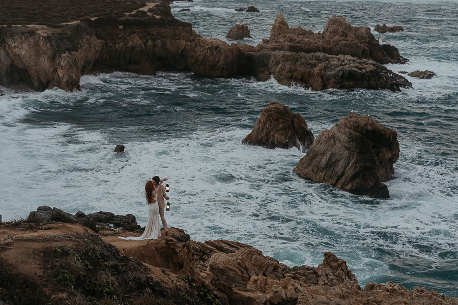 Bride and groom kissing while holding lanterns on a bluff over the ocean in Big Sur