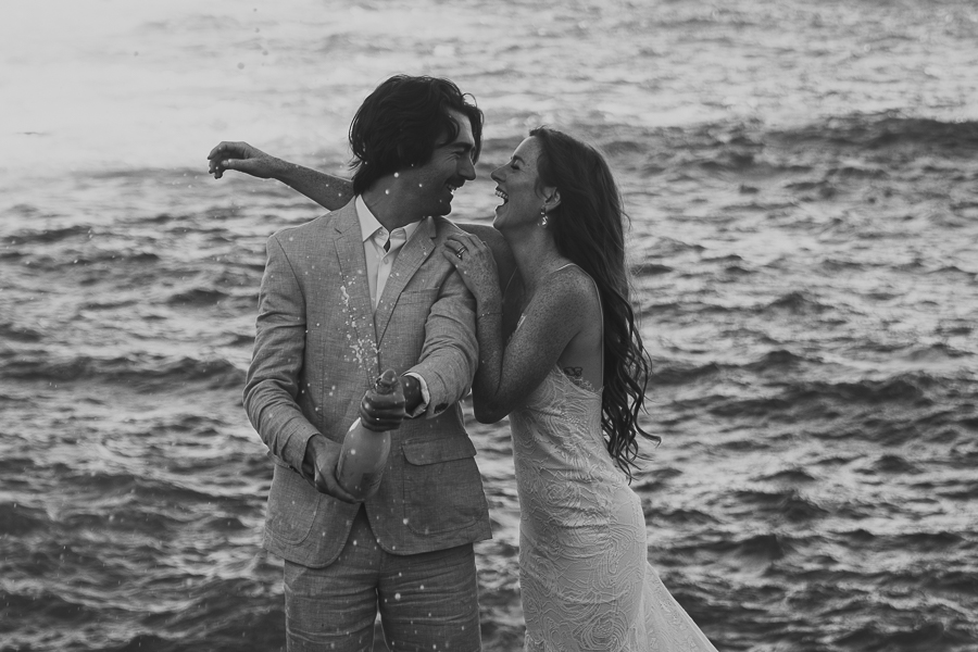Black and white photo of bride and groom looking at each other with huge smiles while spraying champagne to celebrate their elopement in Big Sur