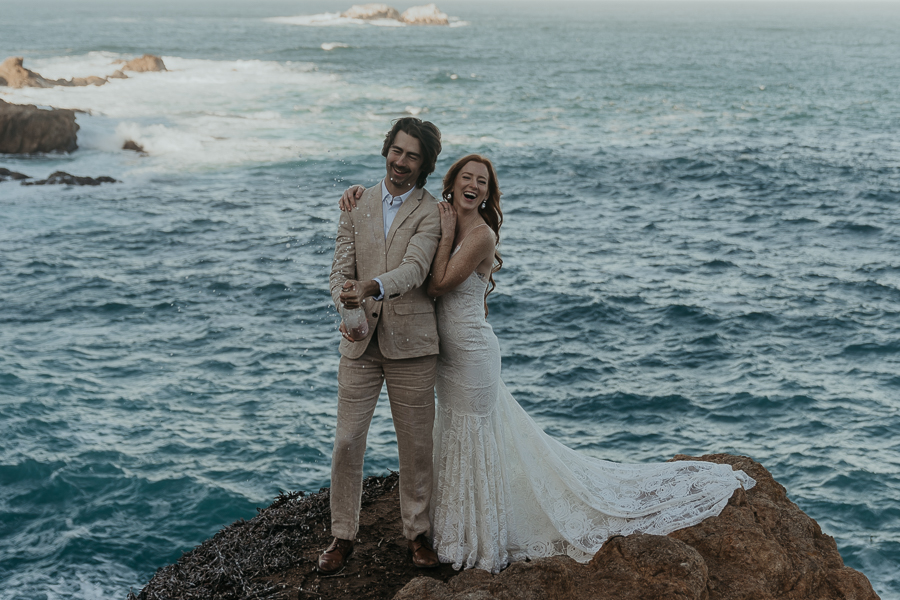 Bride and groom wearing wedding attire pop champagne to celebrate their elopement in Big Sur