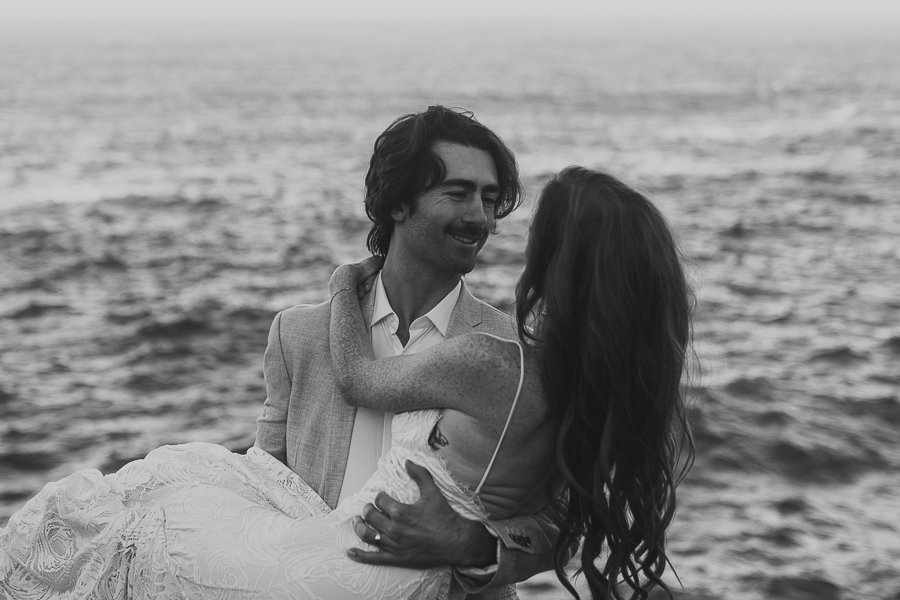 Black and white photo of bride and groom holding bride while looking at each other with ocean in the background at big sur sunrise elopement
