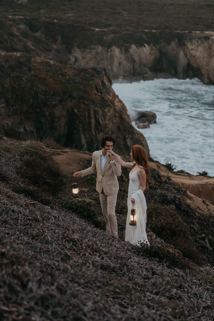 groom kissing brides hand on a bluff trail in Big Sur