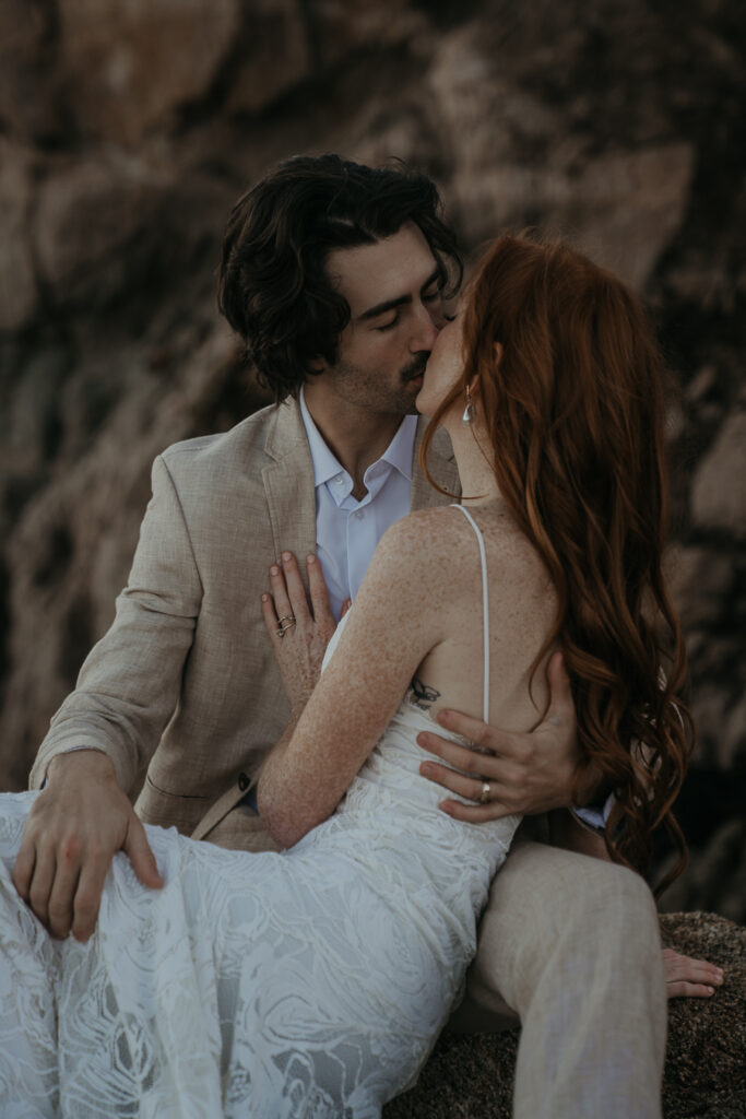 Close up photo of Bride and groom kissing while sitting on rocks