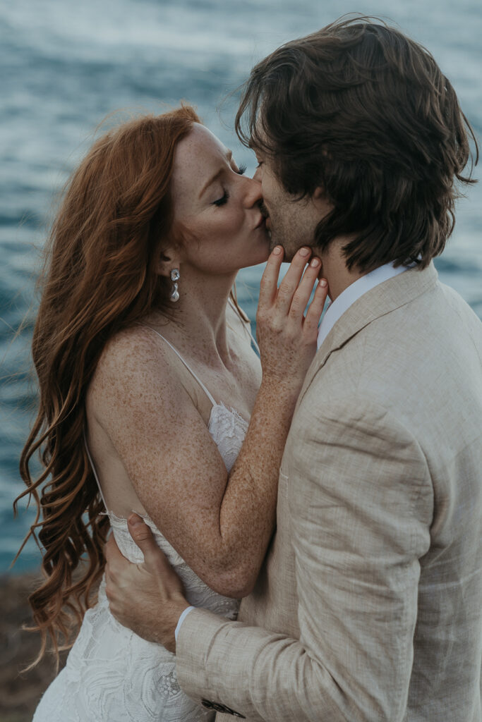 Close up photo of bride and groom kissing with ocean in the background