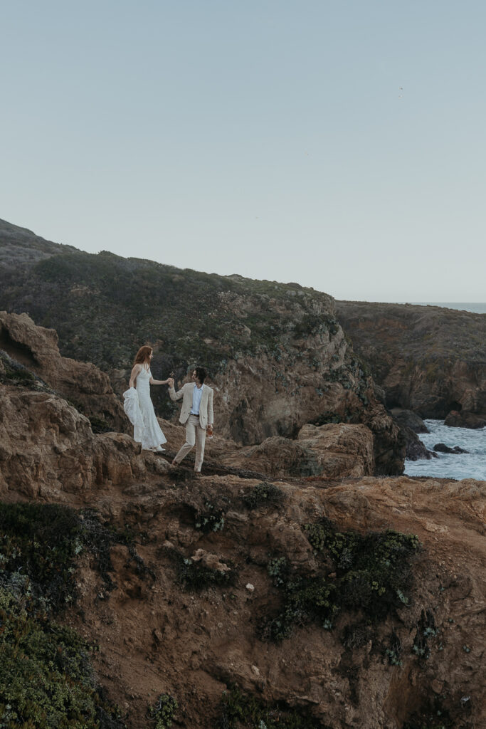 Groom leads bride down rocky coastal trail after elopement in Big Sur