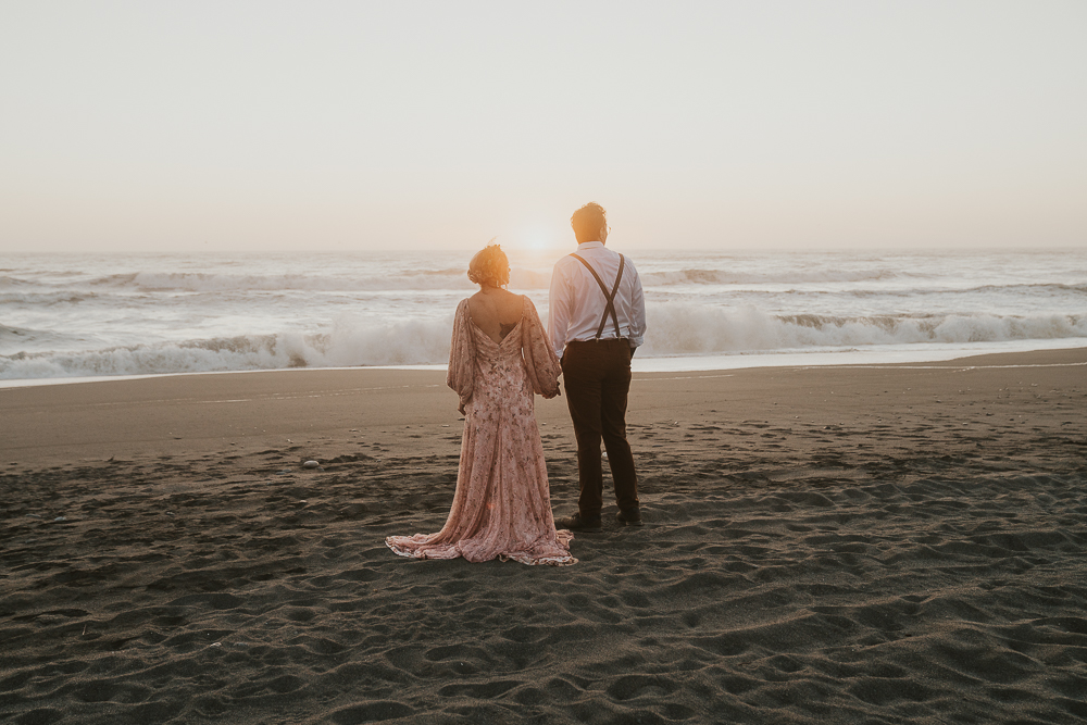 Big Sur elopement photo of bride and groom standing together on beach looking out at the ocean