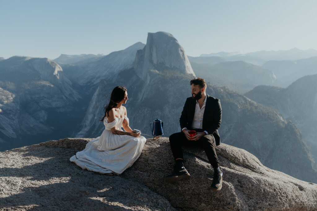 Bride and Groom sitting on a rock in front of Half Dome making coffee together at sunrise after their Yosemite elopement