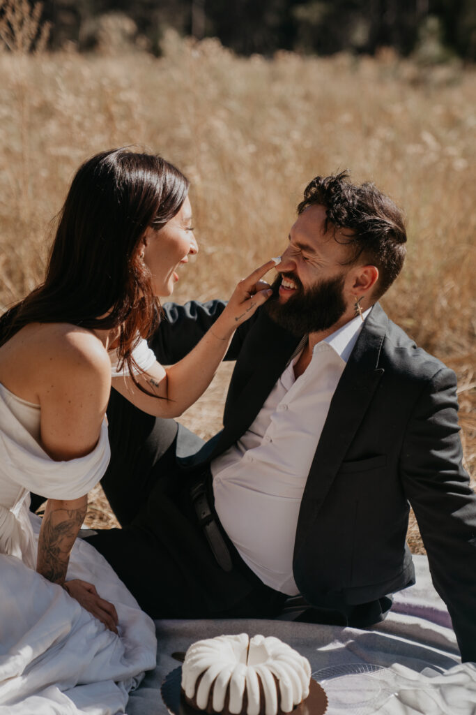 Bride puts frosting on the grooms nose during cake cutting in a meadow