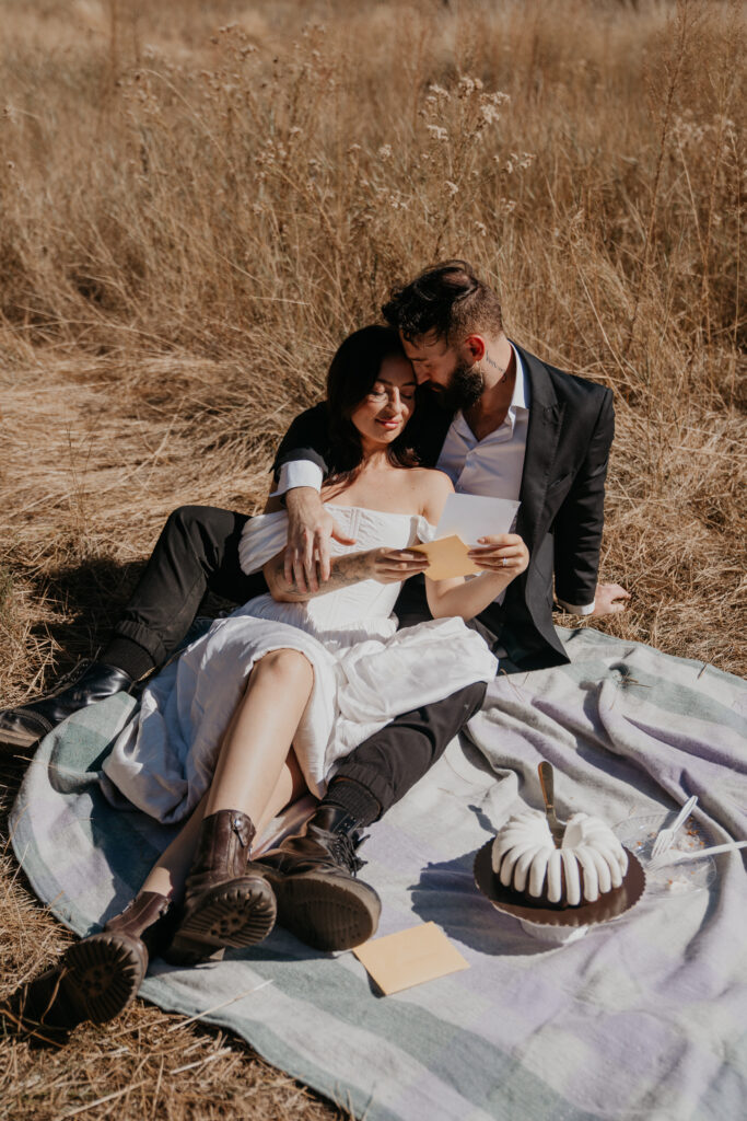 Bride and groom lay together on a picnic blanket reading letters after their elopement in Yosemite